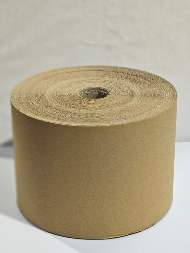A large roll of brown kraft paper tape or wrapping material on a spool, photographed against a neutral light gray background.
